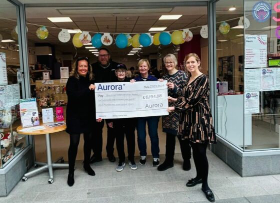 Staff of Aurora Managed Services and Shine A Light stand in front of their store with a Cheque